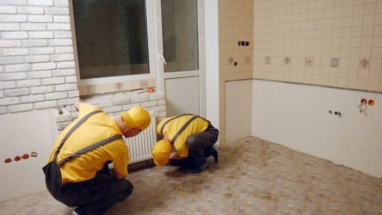 Deux ouvriers en uniformes jaunes installent des panneaux de briques blanches sur un mur d'une pièce carrelée.