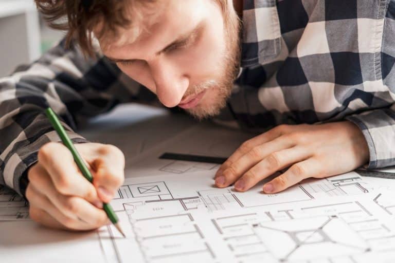 Personne en chemise à carreaux se concentrant sur le dessin de plans architecturaux avec un crayon vert.