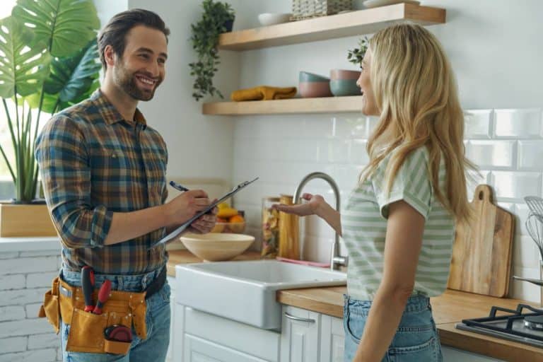 Un bricoleur avec un presse papiers parle à une femme dans une cuisine moderne.