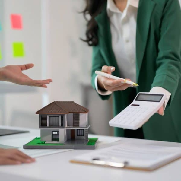 Real Estate Agent Discussing Property Investment with Client Using Calculator and House Model