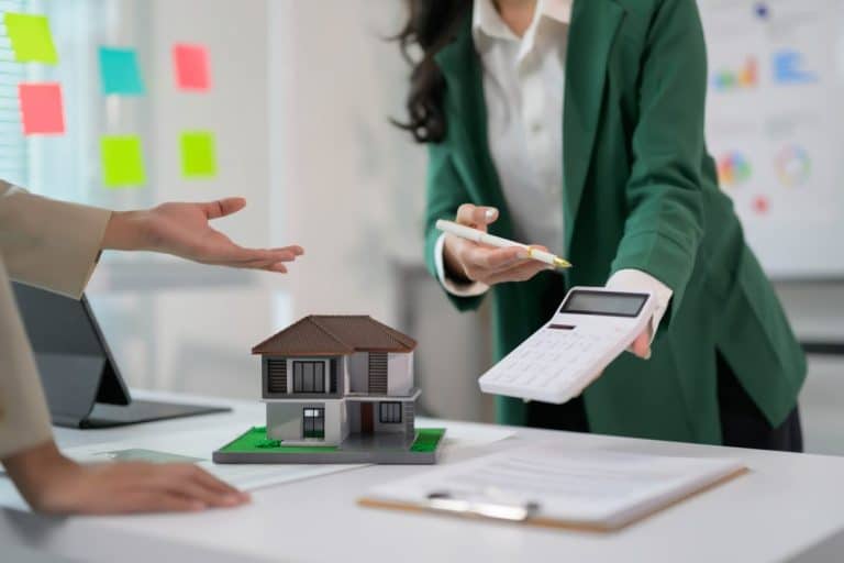 Real Estate Agent Discussing Property Investment with Client Using Calculator and House Model