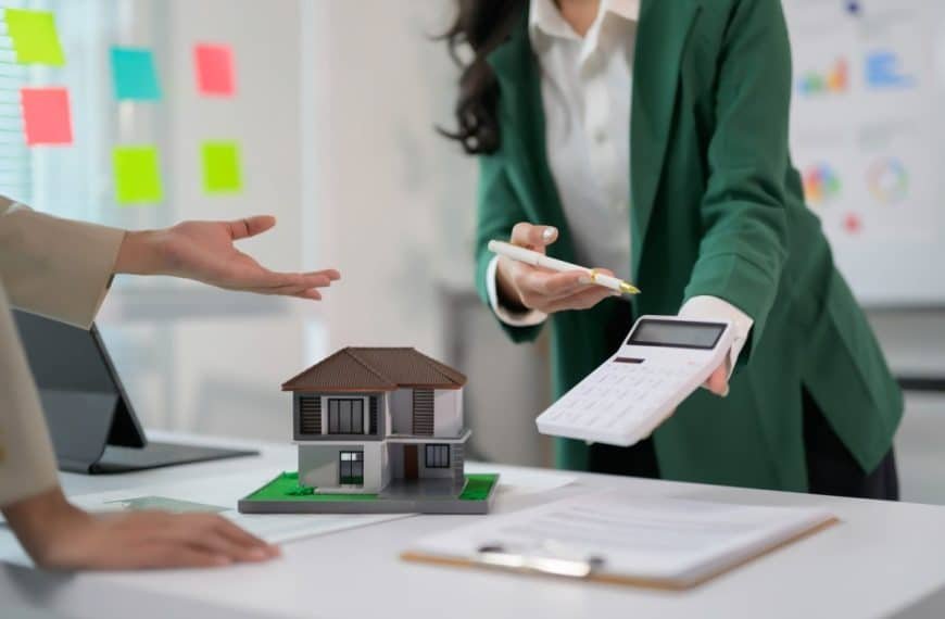 Real Estate Agent Discussing Property Investment with Client Using Calculator and House Model