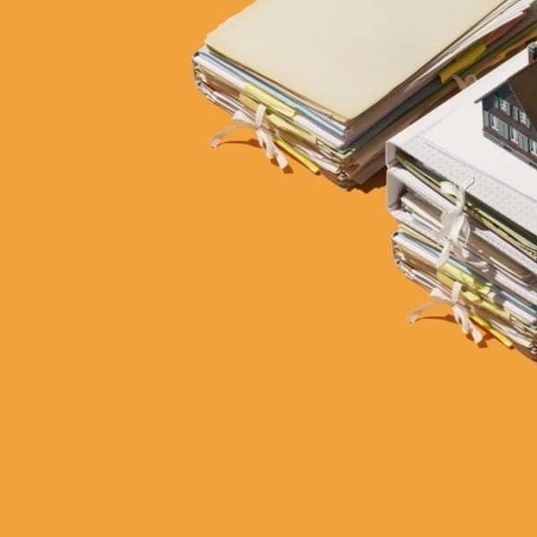 Des piles de dossiers attachés avec des rubans, surmontées d'une petite maquette de maison, sur fond orange.