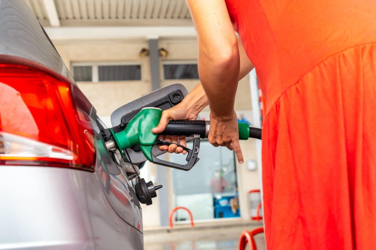 Une personne en robe rouge fait le plein d’essence dans une voiture dans une station service.