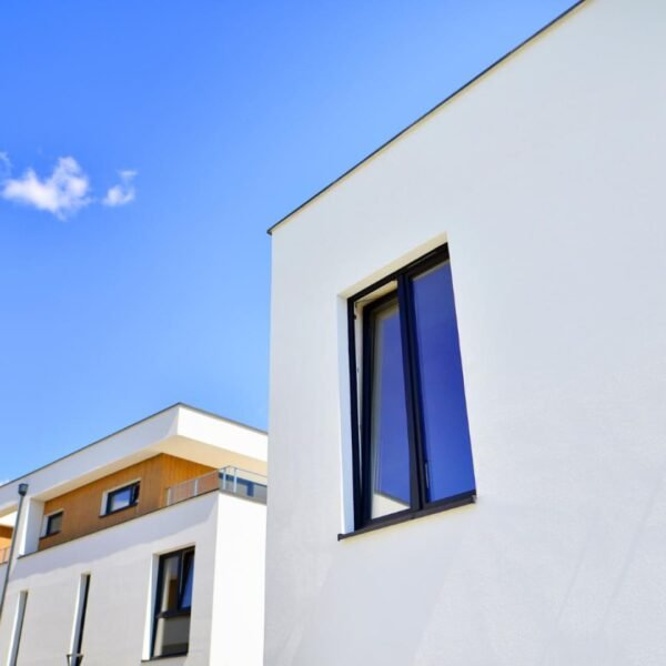 Bâtiments résidentiels modernes blancs avec de grandes fenêtres sous un ciel bleu clair, avec quelques nuages visibles en arrière-plan.