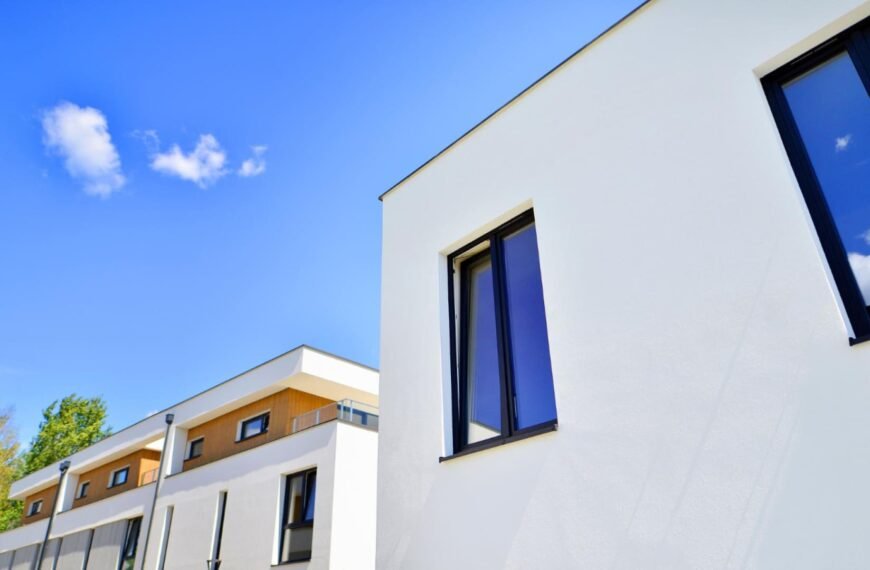 Bâtiments résidentiels modernes blancs avec de grandes fenêtres sous un ciel bleu clair, avec quelques nuages visibles en arrière-plan.