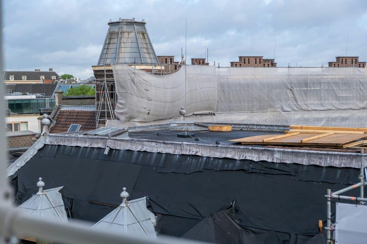 Toiture en cours de rénovation avec échafaudage et couverture de protection. Un ciel nuageux en arrière plan.