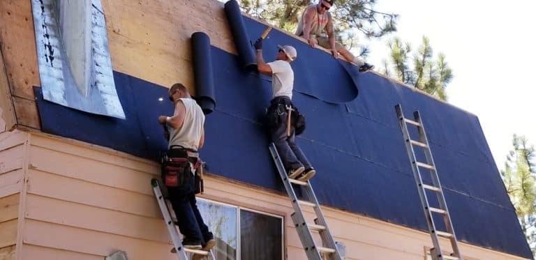 Trois ouvriers du bâtiment sont sur des échelles et installent une nouvelle couche de matériaux de toiture sur une maison.
