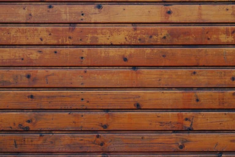 Un gros plan d'un mur en bois composé de planches horizontales. Le bois est teinté d’une couleur brun chaud, présentant divers nœuds et motifs de grain.