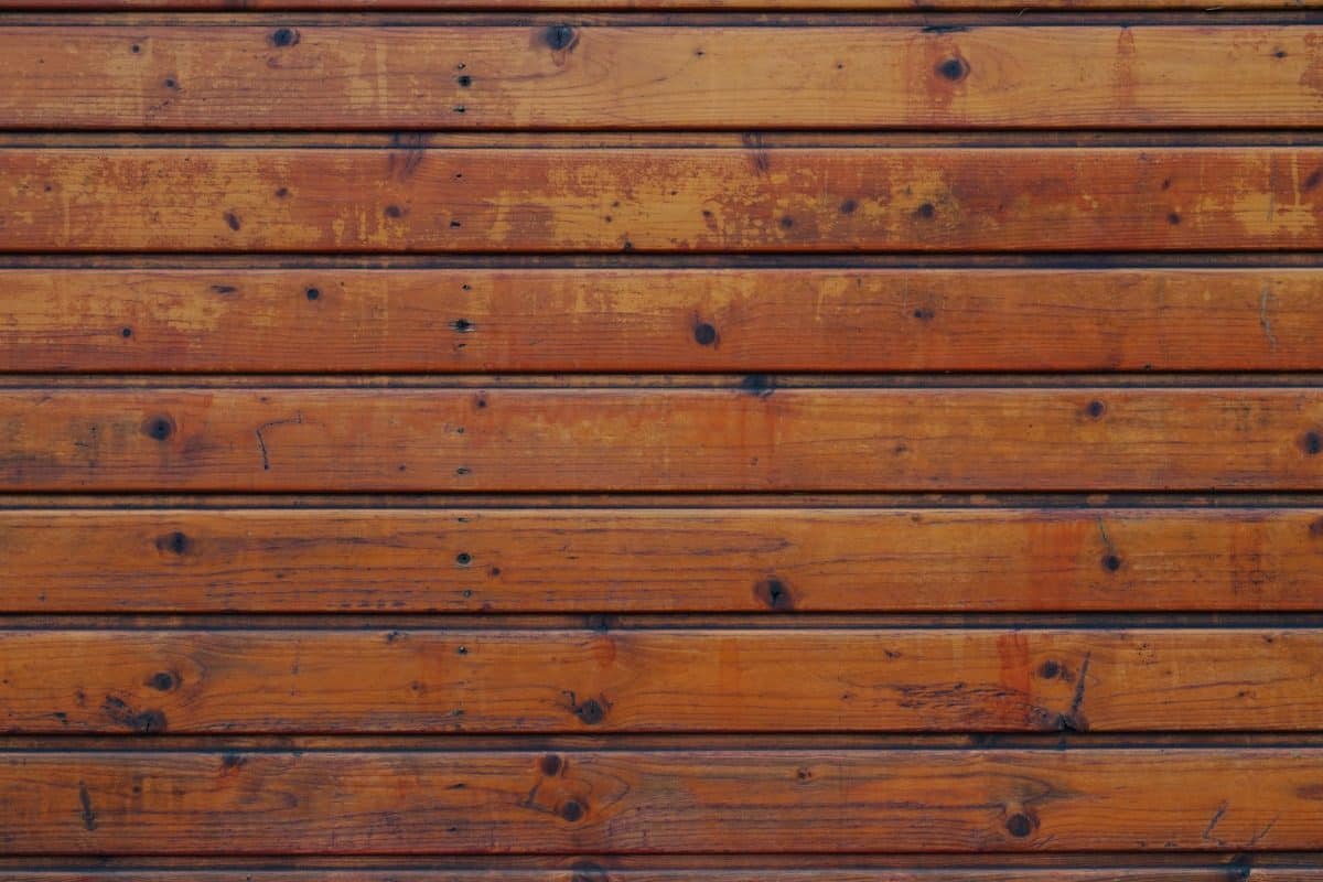 Un gros plan d'un mur en bois composé de planches horizontales. Le bois est teinté d’une couleur brun chaud, présentant divers nœuds et motifs de grain.
