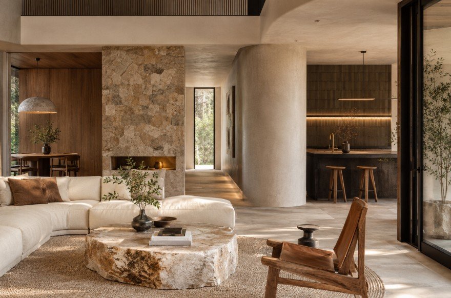 Salon moderne aux tons neutres, avec une table basse en pierre, un canapé modulable blanc, une chaise en bois, une cuisine ouverte et un coin repas, mettant en valeur des textures naturelles et de grandes fenêtres.