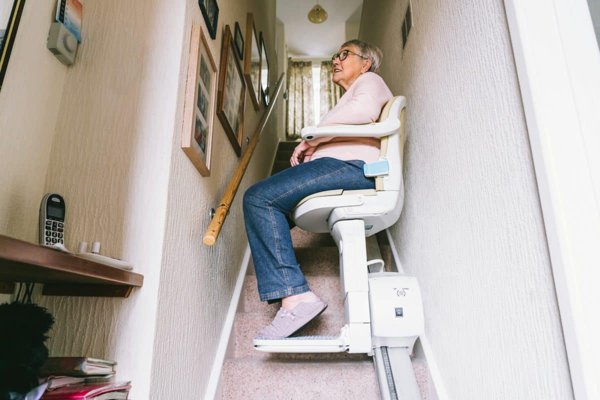 Une femme est assise sur un monte escalier chez elle.