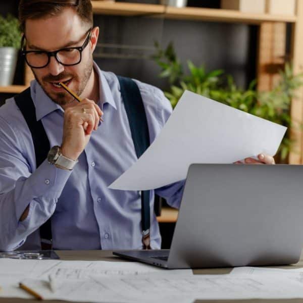 Serious young architect working with laptop and diagramas to construct new building.