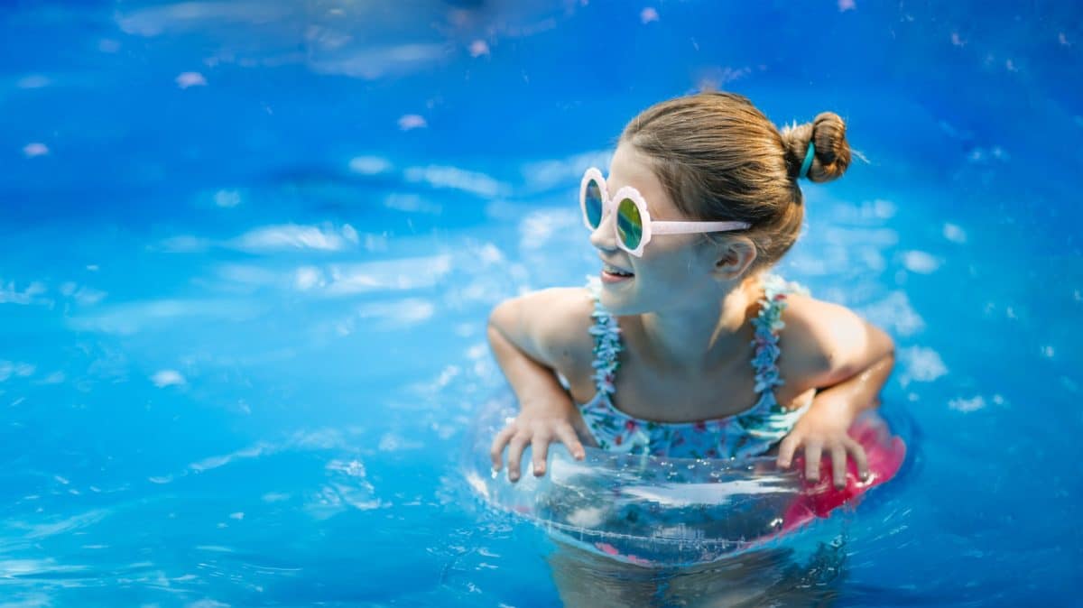 Stylish preteen kid girl swims with circle in pool. Funny child in pink glasses with shells