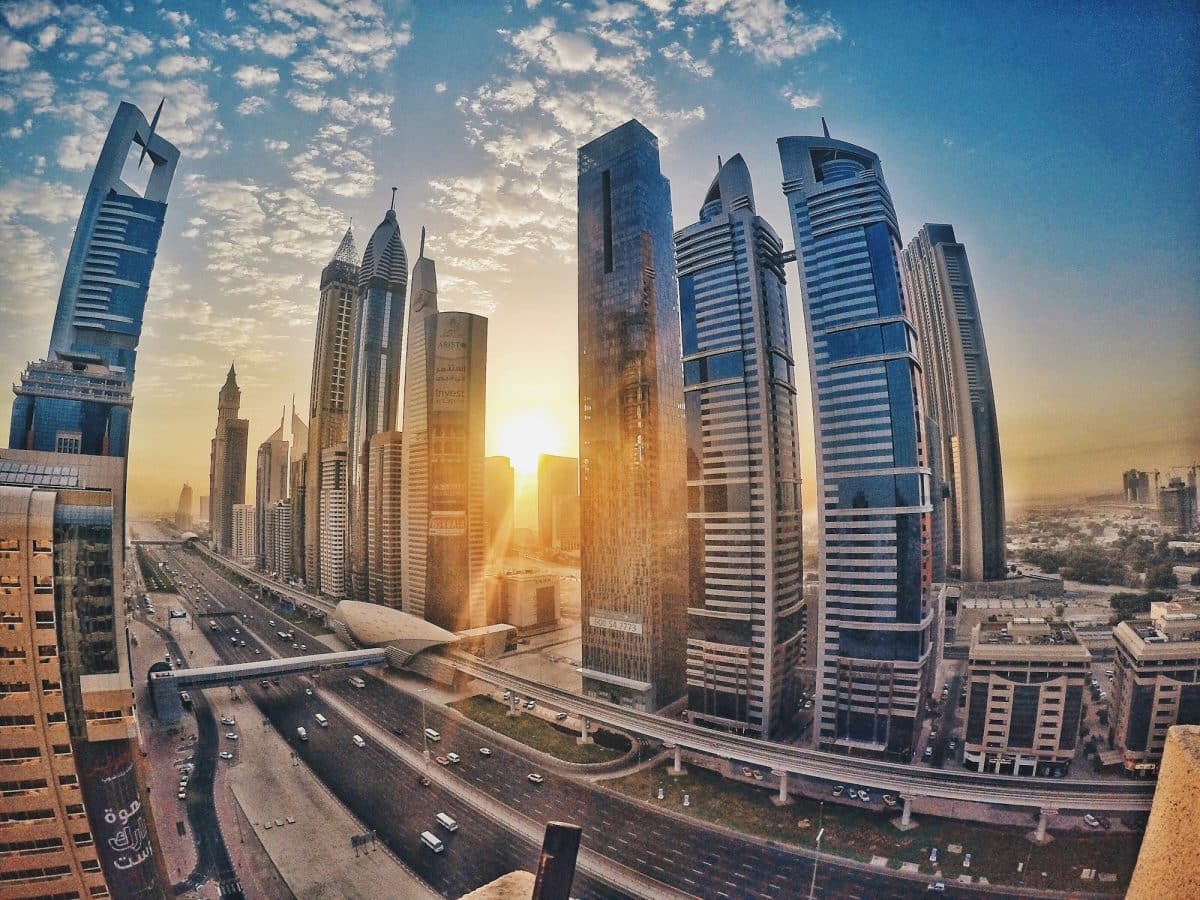 Vue du coucher de soleil sur un paysage urbain avec des gratte-ciels modernes bordant une route très fréquentée sous un ciel partiellement nuageux.