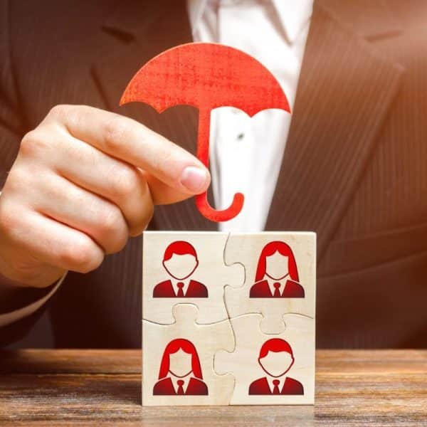 Une main tient une figurine de parapluie rouge au dessus de blocs de puzzle avec des icônes de personnes en costume.