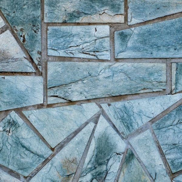 Gros plan d'un motif irrégulier de carreaux de pierre aux nuances variées de bleu et de gris. Les pierres sont disposées selon des formes géométriques, créant un motif fragmenté.