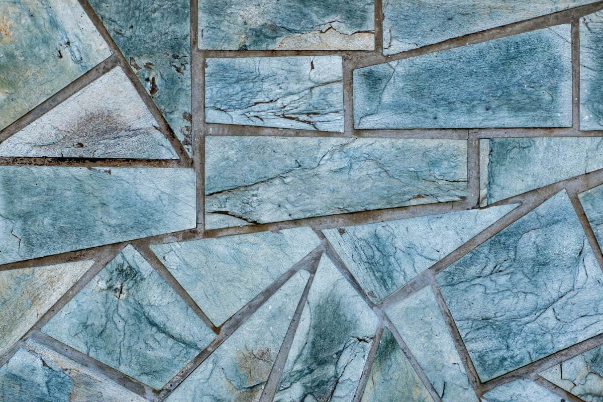 Gros plan d'un motif irrégulier de carreaux de pierre aux nuances variées de bleu et de gris. Les pierres sont disposées selon des formes géométriques, créant un motif fragmenté.