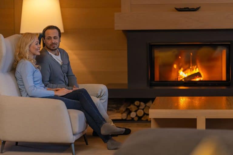 Un homme et une femme sont assis ensemble sur un canapé dans un salon confortable, se tenant par la main et discutant à côté d'une cheminée allumée.