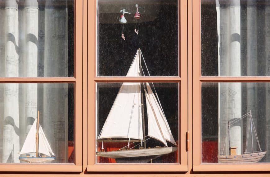 Trois modèles de voiliers exposés sur un rebord de fenêtre avec des rideaux lumineux en arrière plan.