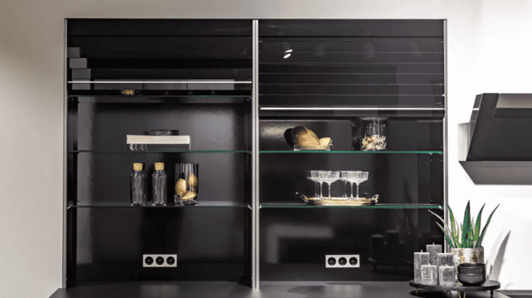 Deux vitrines à étagères en verre, dont l'intérieur est noir, exposent des bouteilles, de la verrerie, des livres et des objets décoratifs. De petites plantes et des tasses sont disposées sur un comptoir situé en dessous. Des prises électriques sont visibles à l'intérieur.