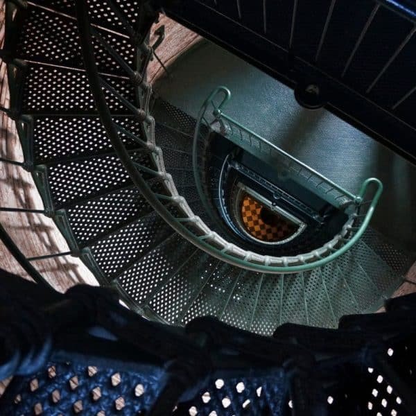 Vue plongeante sur un escalier métallique en colimaçon avec un sol en damier en bas.