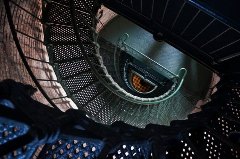 Vue plongeante sur un escalier métallique en colimaçon avec un sol en damier en bas.