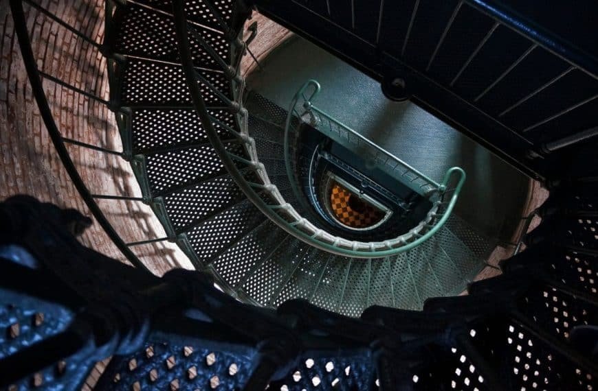 Vue plongeante sur un escalier métallique en colimaçon avec un sol en damier en bas.