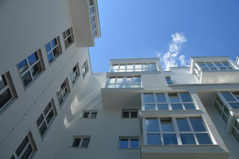 Vue vers le haut d'un immeuble d'appartements moderne et blanc avec de nombreuses grandes fenêtres dans un ciel bleu clair.