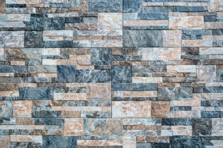 Un mur détaillé composé de dalles de pierre rectangulaires imbriquées dans différentes nuances de gris et de marron.