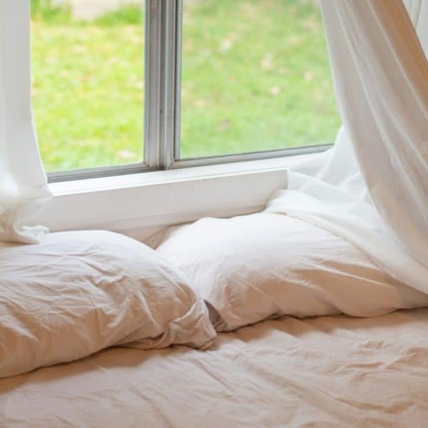 Linge de lit blanc sur le lit près de la fenêtre avec des rideaux blancs. Design minimaliste