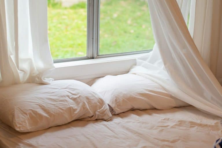 Linge de lit blanc sur le lit près de la fenêtre avec des rideaux blancs. Design minimaliste