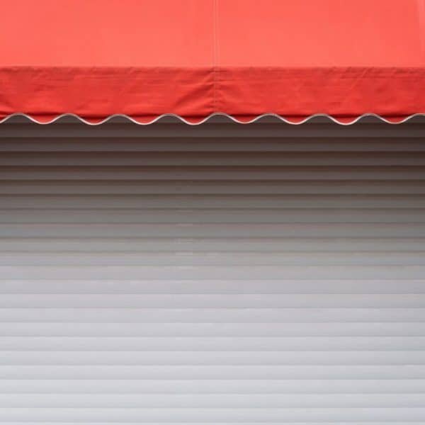 Un auvent rouge s'étend sur une porte à enroulement en métal blanc fermée.