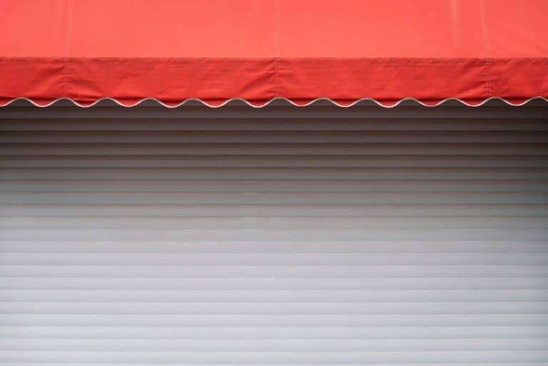 Un auvent rouge s'étend sur une porte à enroulement en métal blanc fermée.