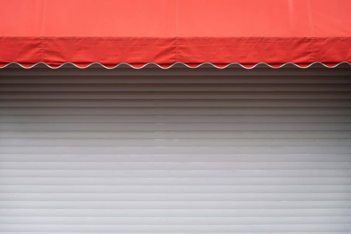 Un auvent rouge s'étend sur une porte à enroulement en métal blanc fermée.