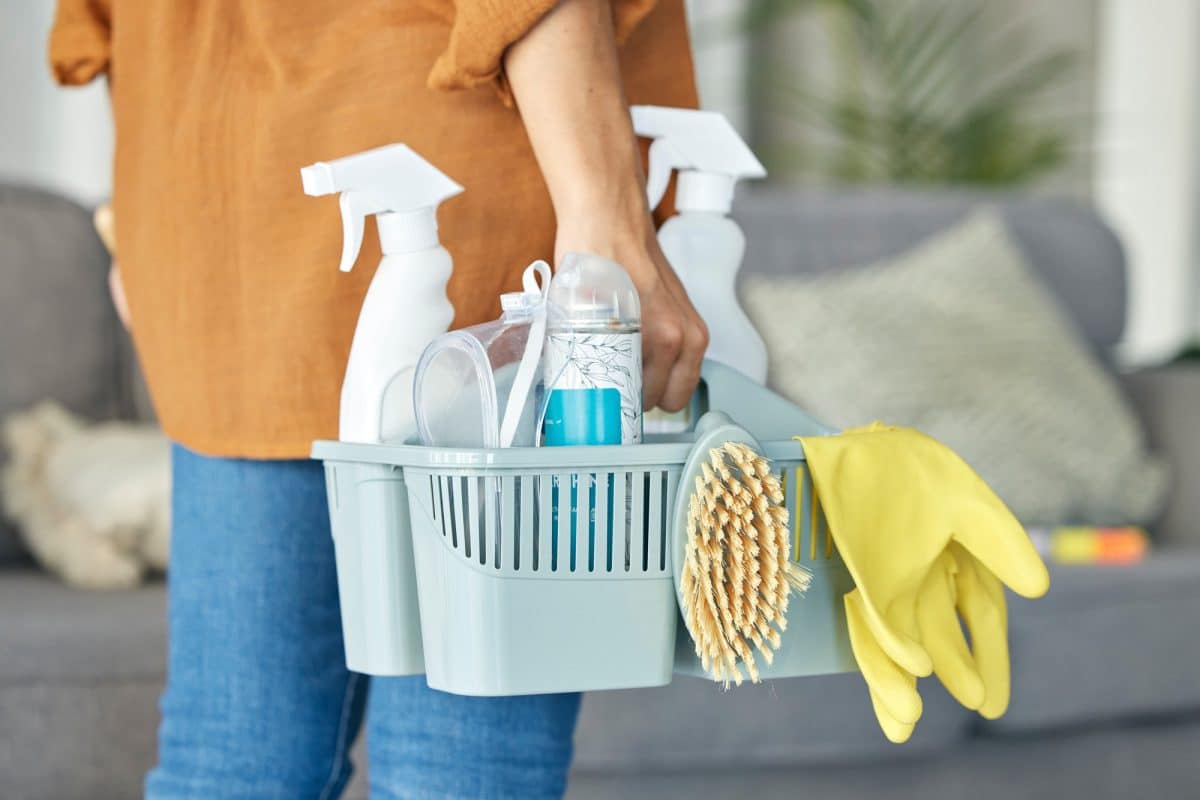 Une femme tenant un panier rempli de produits de nettoyage.