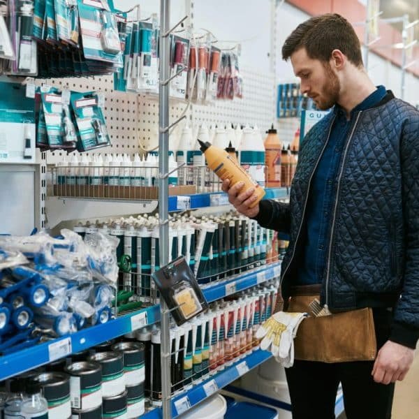 Un homme portant une veste matelassée et une ceinture à outils examine une bouteille alors qu'il se tient dans l'allée d'une quincaillerie.