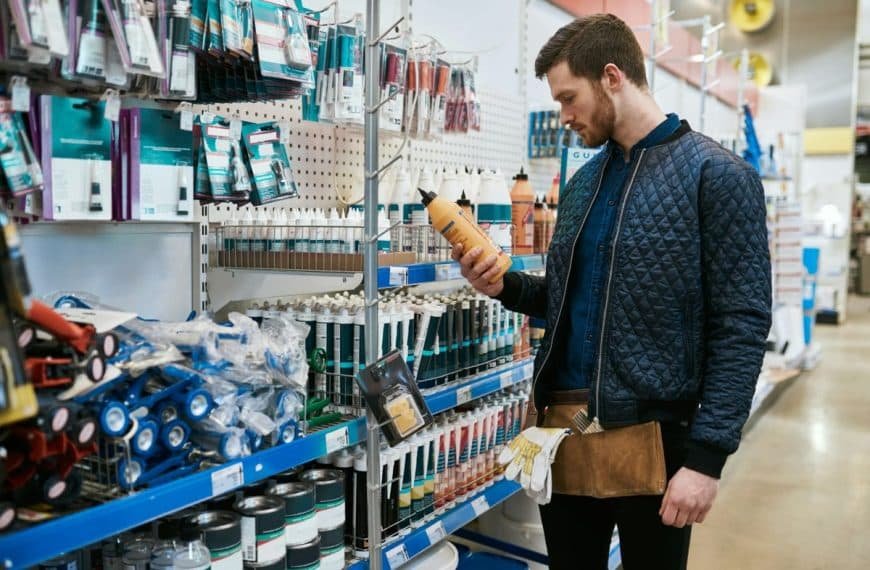 Un homme portant une veste matelassée et une ceinture à outils examine une bouteille alors qu'il se tient dans l'allée d'une quincaillerie.